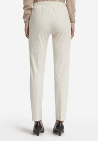Pantaloni beige chiaro con vita elastica e design affusolato. Texture liscia, senza motivi visibili, abbinati a scarpe col tacco scure.