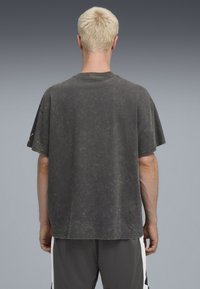 Sort, oversized t-shirt med korte ærmer og en falmet, slidt struktur. Har rund halsudskæring og let opslåede ærmer.