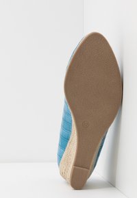 Semelle d'une chaussure compensée bleue tissée avec une semelle en caoutchouc beige texturée, taille 37, photographiée sur fond blanc dans un coin.