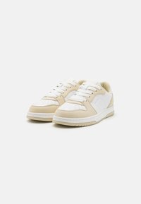 Beige and white sneakers featuring leather and suede materials, round toe, perforations on the toe box, and flat white laces.