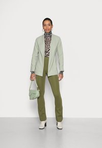 Blazer verde menta sobre um suéter de gola alta com padrão de leopardo, combinado com calças verde-azeitona. Botas de cano curto brancas e uma bolsa menta a condizer.