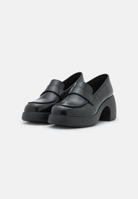 Chaussures en cuir verni noir avec un bout arrondi, une large sangle sur le devant et un talon épais et courbé. Texture lisse et design épuré.