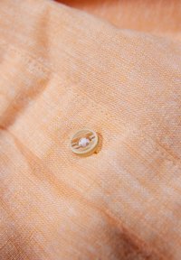 Tessuto arancione chiaro con una superficie testurizzata, con un bottone circolare giallo pallido dotato di un dettaglio di cucitura centrale.