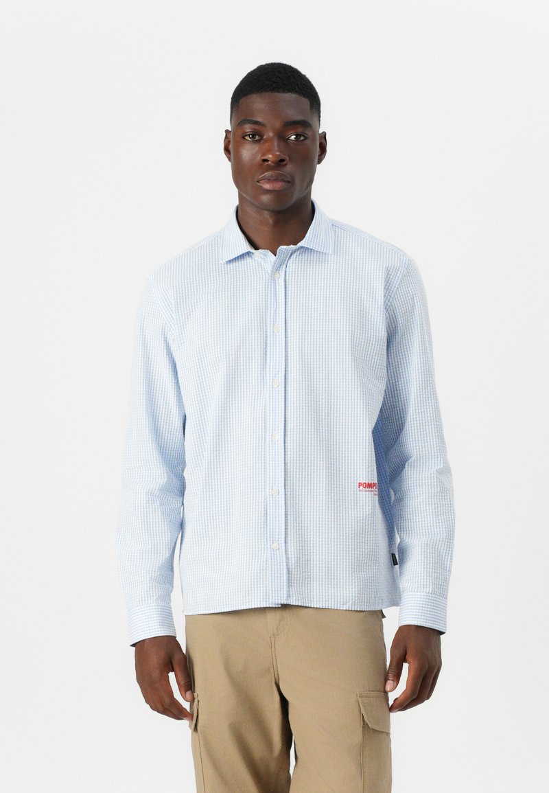 Blue and white checkered button-up shirt with long sleeves, featuring a visible red logo on the left side and a softened collar design.