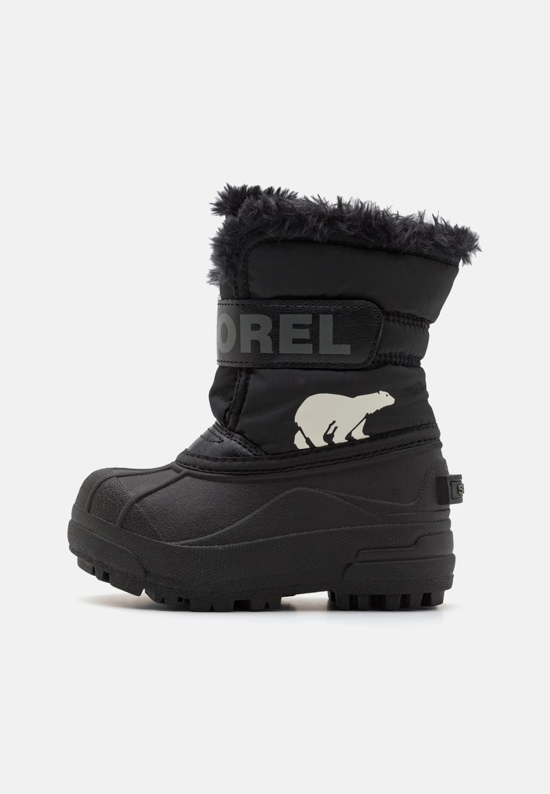 Botas de invierno negras con un exterior texturizado, material sintético, cuello de forro polar, correa con logo prominente y detalle gráfico de un oso. Suela de goma flexible.