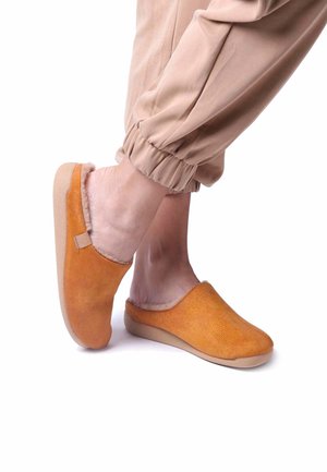 Orange mockasiner i mocka med mjukt, fluffigt foder; enkel design att sätta på sig; beige gummisula; slät textur; rundade tår; minimala detaljer.