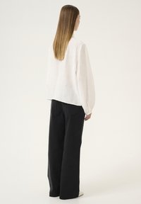 Cremefarvet bluse med struktur og lange ærmer, parret med sorte, vide bukser. Outfittet er enkelt med minimal detaljering, velegnet til hverdag.