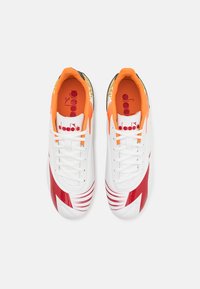 Pár bílých sportovních bot Diadora s červenými a oranžovými akcenty, pohled zhora, s bílými tkaničkami a oranžovými vkládacími stélkami s logem.
