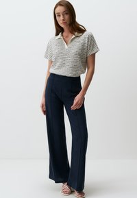 Biała koszulka polo z krótkim rękawem i teksturowanym granatowym wzorem, w połączeniu z granatowymi spodniami o szerokich nogawkach z wysokim stanem i przeszyciami z przodu.