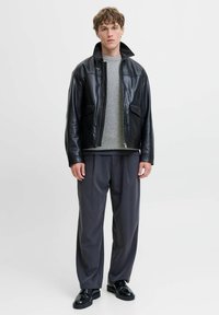 Veste en cuir noir avec un col haut, associée à un pull gris et un pantalon gris ample. Des chaussures noires complètent la tenue.