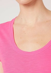 Camiseta de manga corta de color rosa brillante con un amplio escote redondeado, hecha de una tela suave y texturizada. Presenta un aspecto ligeramente jaspeado.