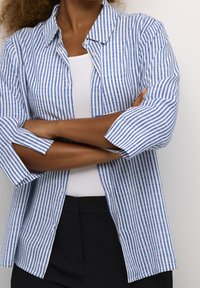 Blue and white striped button-up shirt with a collar, long sleeves rolled up, made of lightweight fabric, featuring a relaxed fit design.