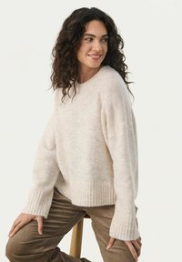 Pull crème à la finition douce et texturée, avec des poignets et un ourlet à larges côtes, et une coupe décontractée. Associé à un pantalon en velours côtelé marron.