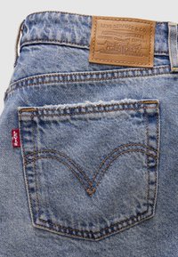 Πίσω τσέπη από ανοιχτόχρωμα τζιν Levi's με πορτοκαλί ραφές, κόκκινη ετικέτα Levi's και καφέ δερμάτινο σήμα της μάρκας πάνω από τη μέση.