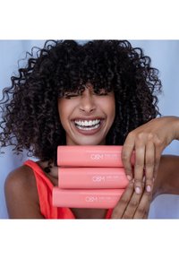 Three cylindrical, coral-colored hair product tubes labeled "O&M Curl Curl" stacked together. The tubes have a matte finish and white text.