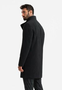 Abrigo negro de lana con un alto cuello y un corte ajustado, que presenta una textura suave y un diseño minimalista, mostrado desde la parte trasera.
