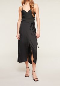 Černá saténová sukni s vysokým rozparkem, s páskem na zavázání v pase a zvýrazněnými švy. V kombinaci s přiléhavým černým ribbed topem.