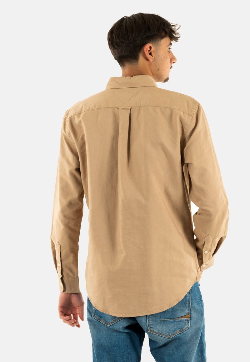 Lange mouwen, licht beige shirt met een rugplooien, knoopmanchetten en afgeronde zoom, gecombineerd met blauwe jeans. Katoen of een vergelijkbaar materiaal.