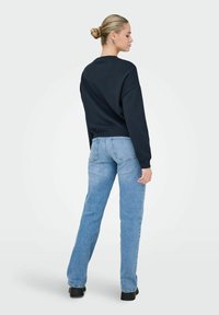 Sweatshirt oversize bleu marine à manches longues associé à un jean droit bleu clair. Des chaussures compensées noires complètent la tenue.