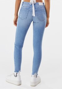 Jeans ajustados de mezclilla azul claro con una cintura alta, dobladillo deshilachado y bolsillos traseros. Combinados con zapatillas blancas y calcetines estampados.