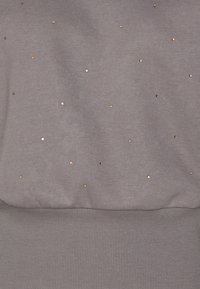 Felpa grigia con paillettes sparse su tutto il tessuto. L'orlo e i polsini a coste contrastano con la texture liscia del corpo.