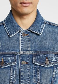 Jeansjacka i medelblått med en klassisk design, som har en spetsig krage, två bröstfickor och metallek, knappar i kopparfärg.