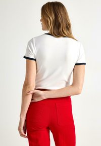 Witte t-shirt met korte mouwen en marineblauwe accenten, slim fit ontwerp, gladde textuur, gecombineerd met hooggelegen rode broek.