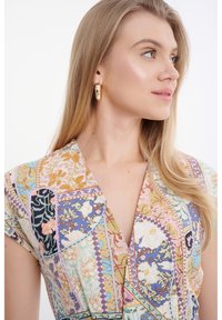 Geprinte jurk met een V-hals, voorzien van bloem- en geometrische patronen in pastelkleuren. Gemaakt van lichte stof. Details van gouden creolen.