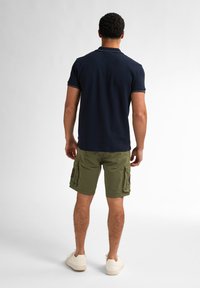 Navy polo shirt with short sleeves paired with olive green cargo shorts featuring side pockets, worn with white sneakers.