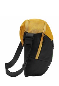 Zwarte en gele schoudertas van een gestructureerde stof, met een ritssluiting, verstelbare band en een zijaccent met licht. Compakte en hoekige vormgeving.
