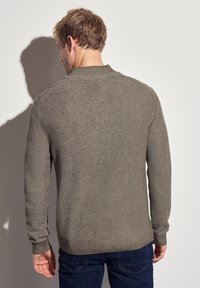 Pull en maille marron avec un col, des poignets et un ourlet côtelés. Présente un tissu texturé et un design simple et classique.