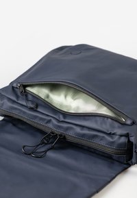 Marineblaue Tasche aus glattem, wasserabweisendem Material. Hervorhebung mit einem großen Reißverschlussfach mit hellgrüner Innenausstattung und doppelten Reißverschlusslaschen für einfachen Zugriff.