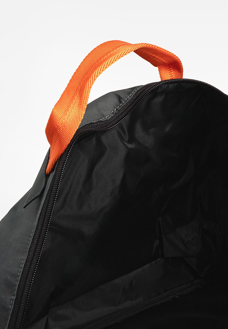 Sac en tissu noir avec une poignée en nylon orange, fermeture éclair et intérieur lisse. Ne présente pas de poches externes ni de matériel visible.