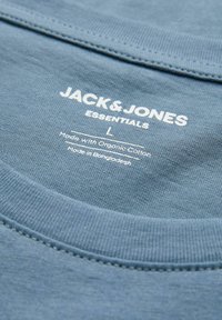 Το γιακά ενός μπλουζάκι Blue Jack & Jones Essentials που δείχνει ετικέτα με μέγεθος large, φτιαγμένο από οργανικό βαμβάκι, κατασκευασμένο στο Μπαγκλαντές.