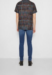 Camicia a maniche corte, con motivo in tonalità scure e design a quadri colorato, abbinata a jeans blu aderenti e stivaletti neri alla caviglia.