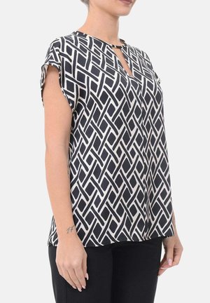 Vrouw draagt een kortemouw zwarte-wit geometrisch patroon blouse met een klein sleutelgatsluiting aan de voorkant, gecombineerd met zwarte broek.