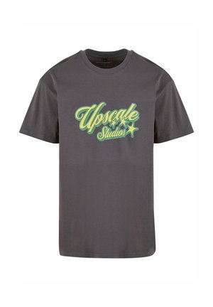 Grå bomulds t-shirt med korte ærmer og rund halsudskæring. Har "Upscale Studios" i stiliseret grøn og gul skrift på forsiden.