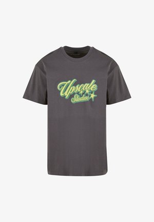Szürke pamut póló rövid ujakkal és kerek nyakkivágással. Az elején stilizált zöld és sárga betűkkel van írva: "Upscale Studios".