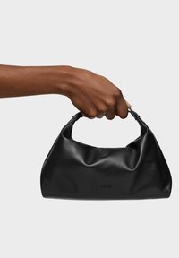 Bolso de mano de cuero negro con textura suave y arrugada, con un asa curvada. Logo grabado en la parte delantera, diseño minimalista.