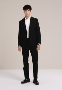 Czarny garnitur o dopasowanym kroju, biała koszula i błyszczące czarne buty. Gładka faktura, klasyczny design i dopasowany wygląd.