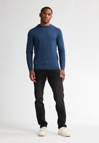 Pulover lung cu dungi orizontale, texturat, de culoare bleumarin, purtat cu blugi negri și adidași albi. Design simplu și ajustat.
