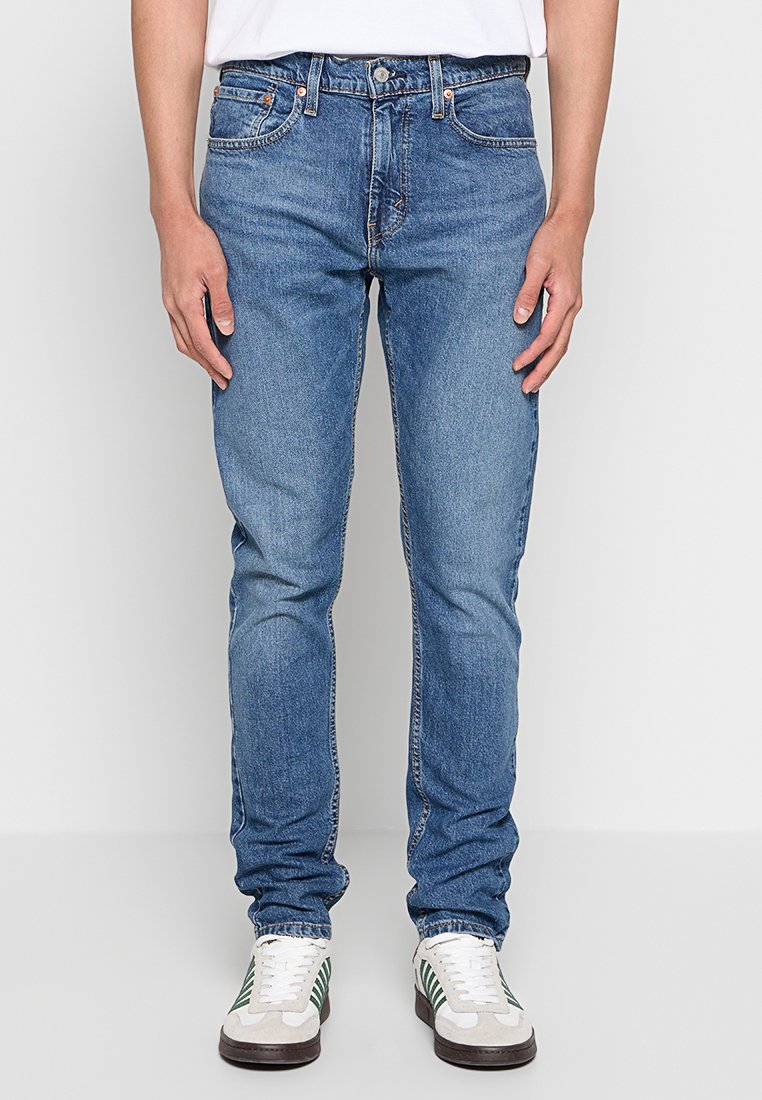 Hellblaue Denim-Jeans im Slim-Fit mit fünf Taschen und dezenten Waschungen. Getragen mit weißen und grünen Sneakern.