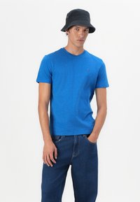 Blauwe ronde hals t-shirt van gladde katoen, gecombineerd met donkerblauwe jeans. Het t-shirt heeft een klein logo op de borst.