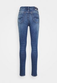 Jeans ajustados de mezclilla azul medio, con cintura alta, textura desgastada y dos bolsillos traseros con detalles de costura curva.