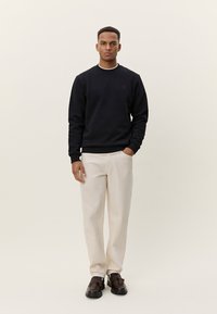 Μαύρο βαμβακερό φούτερ με λευκή λαιμόκοψη, κρεμ παντελόνια και καφέ παπούτσια. Απλός σχεδιασμός με διακριτική λεπτομέρεια λογότυπου στο στήθος.