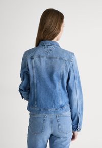 Denim jakk featuring kerge sinine pesu, klassikaline krae, pikad varrukad ja nööbiga mansetid. Seljal on õmblusteta detail ja õmmeldud õmblused.