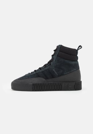 Czarne zamszowe sneakersy za kostkę z wyściełanym siateczkowym kołnierzem, sznurowaniem z przodu, teksturowaną gumową podeszwą i napisem "SAMBA" z boku.