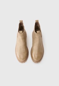 Une paire de bottines chelsea en cuir beige à enfiler avec des tirettes et des semelles en caoutchouc nervurées sur un fond blanc.