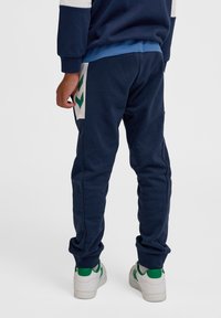 Marineblauwe joggingbroek met elastische boorden en een zijpaneel met een groen zigzagontwerp. Gepaard met witte sneakers met groene accenten.