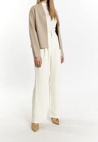 Béžová krátká bunda přes bílou košili, doplněná krémovými širokými kalhotami a béžovými špičatými lodičkami. Hladká tkanina a minimalistický design.